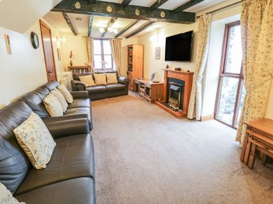 A living room with two leather sofas a fireplace a wall-mounted television wooden furniture and curtains at Bank End Barn Grizebeck