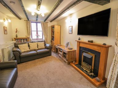 A living room with leather sofas a wooden fireplace a wall mounted television and bookshelves at Bank End Barn in Grizebeck