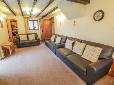 A sitting room with leather sofas cushions wooden furniture and exposed ceiling beams at Bank End Barn in Grizebeck