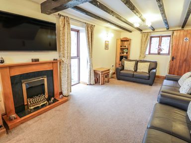 A living room with two sofas a fireplace a wall mounted TV and wooden beams on the ceiling at Bank End Barn in Grizebeck