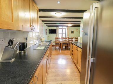A kitchen with wooden cabinets black countertops a stainless steel refrigerator and a dining area with a table and chairs at Bank End Barn in Grizebeck