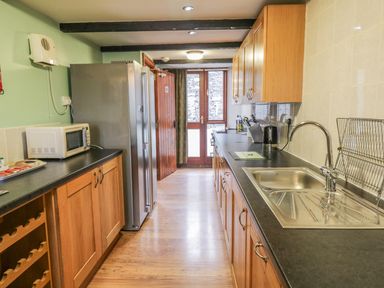 A narrow kitchen with wooden cabinets a stainless steel sink a microwave and a refrigerator at Bank End Barn in Grizebeck