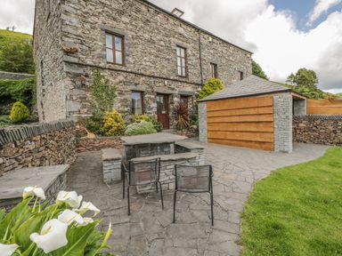 An outdoor stone patio area with two chairs a stone table a wooden shed and stone building at Bank End Barn in Grizebeck
