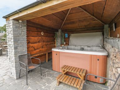An outdoor covered area with a hot tub wooden steps metal chairs stone pillars and wooden bench at Bank End Barn in Grizebeck