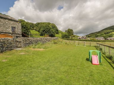 A grassy outdoor area with a small slide and a soccer goal near stone buildings and hills at Bank End Barn in Grizebeck