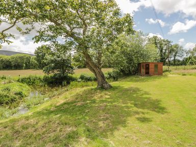 A grassy area with a tree a small pond and a wooden shed at Bank End Barn in Grizebeck
