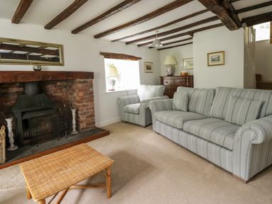 A living room with a striped sofa and armchair a brick fireplace and a wicker coffee table at Hall Bank Cottage in Rydal near Ambleside