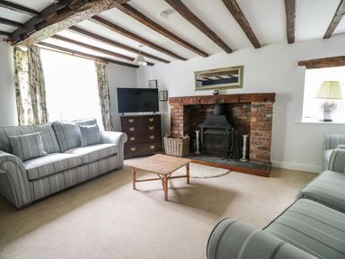 A living room with two sofas a wooden coffee table a brick fireplace and a television on a chest of drawers at Hall Bank Cottage in Rydal near Ambleside