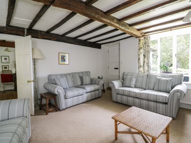 A living room with two striped sofas a wicker coffee table and wooden beams on the ceiling at Hall Bank Cottage Rydal near Ambleside