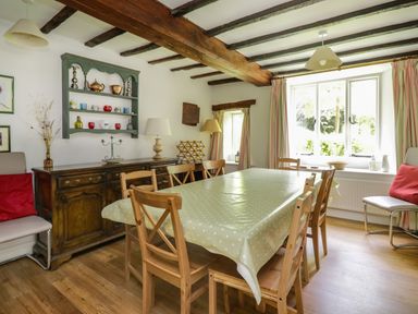 A dining room with a wooden table and chairs near a window at Hall Bank Cottage in Rydal near Ambleside