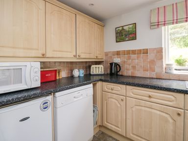 A kitchen with wooden cabinets a microwave a red bread box a toaster an electric kettle and a window at Hall Bank Cottage in Rydal near Ambleside