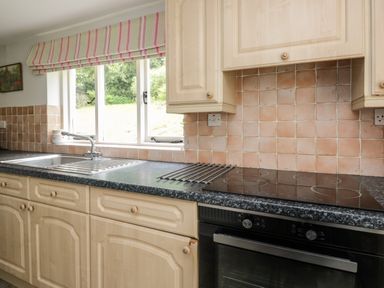 A kitchen counter with sink and stove below cabinets and a window with striped blind at Hall Bank Cottage in Rydal near Ambleside