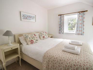A bedroom with a bed with floral pillows and blanket and towels on it at Hall Bank Cottage in Rydal near Ambleside