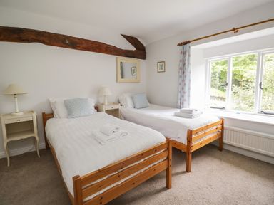 A bedroom with two single wooden beds and bedside tables near a window at Hall Bank Cottage in Rydal near Ambleside