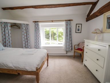 A bedroom with a wooden bed a white dresser a wicker chair and floral curtains at Hall Bank Cottage in Rydal near Ambleside