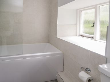 A bathroom with a bathtub a window and a toilet paper holder at Hall Bank Cottage in Rydal near Ambleside