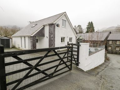 A white house with dark stone accents behind a black wooden gate at Ty Coch in Llanberis