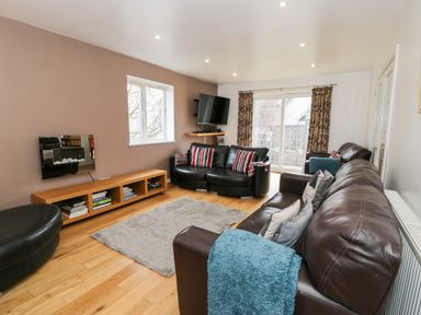 A living room with leather sofas a rug a wall-mounted TV and a wooden low shelf at Ty Coch in Llanberis