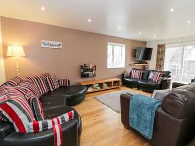 A living room with leather sofas and striped cushions a wooden floor and a wall mounted tv at Ty Coch in Llanberis