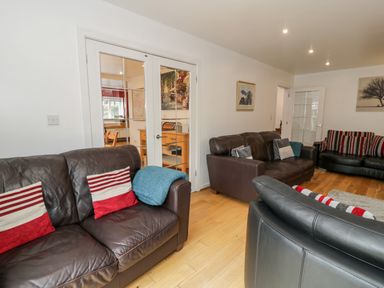 A living room with three brown leather sofas pillows and glass doors leading to another room at Ty Coch in Llanberis
