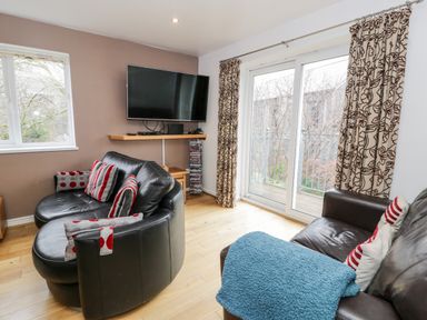 A living room with black leather sofas with red and grey pillows a mounted TV and a sliding glass door at Ty Coch in Llanberis