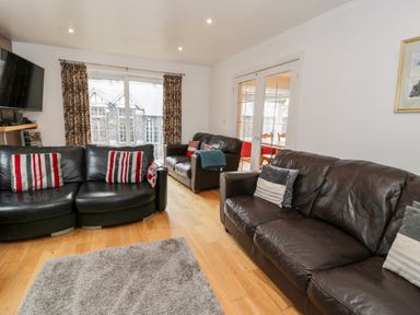 A living room with three leather sofas a gray rug curtains on a window and a wall-mounted TV at Ty Coch in Llanberis
