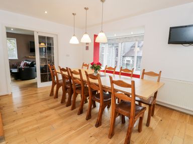 A dining room with a long wooden table and chairs a window and a wall-mounted television at Ty Coch in Llanberis
