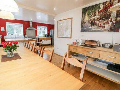 A dining table with wooden chairs and a vase of red roses in a kitchen with red walls and wooden cabinets at Ty Coch in Llanberis
