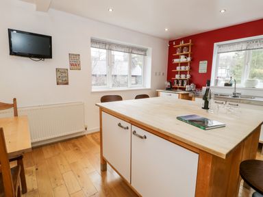 A kitchen with a large island table wooden floor and red accent wall at Ty Coch in Llanberis
