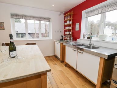A kitchen with wooden floor cabinets and two windows with patterned blinds at Ty Coch in Llanberis