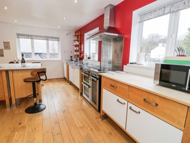 A kitchen with wooden floors wooden and white cabinets a stove a microwave and a bar stool at Ty Coch in Llanberis