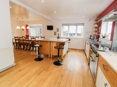 A kitchen with an island and two stools next to a dining area with a long wooden table and chairs at Ty Coch in Llanberis
