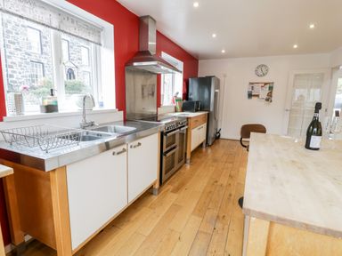 A kitchen with wooden floors stainless steel countertops a stove a refrigerator and a wooden island at Ty Coch in Llanberis