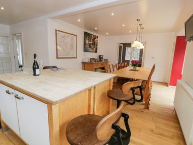 A dining room with a island counter with bar stools and a long dining table with chairs at Ty Coch in Llanberis