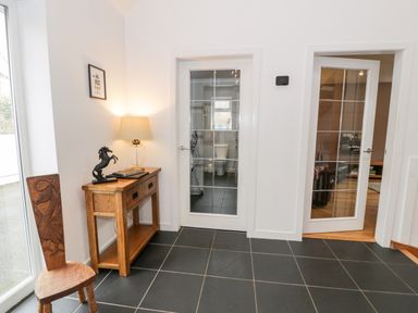 An entryway with a wooden chair and a wooden console table with a lamp and horse statue next to glass doors at Ty Coch in Llanberis