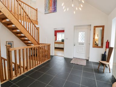 An entryway with black tiled floor wooden staircase a white door a mirror a chair and a view into a kitchen at Ty Coch in Llanberis