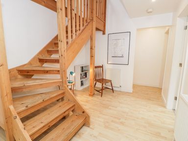 A hallway with wooden stairs a wooden chair a small white bookshelf and a framed picture on the wall at Ty Coch in Llanberis