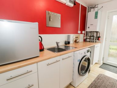 A utility room with a mini fridge, sink, washing machine, boiler, kettle, and cabinets at Ty Coch in Llanberis