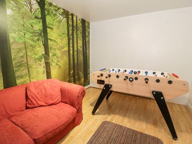A room with a red sofa a foosball table and a forest mural on the wall at Ty Coch in Llanberis