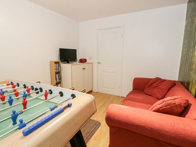 A room with a foosball table a red sofa a small tv on a cabinet and a door at Ty Coch in Llanberis