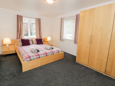 A bedroom with a double bed with plaid bedding two bedside lamps and a wooden wardrobe at Ty Coch in Llanberis