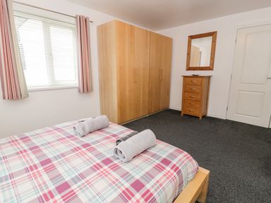 A bedroom with a bed, a wardrobe, a chest of drawers, a mirror, and a window with blinds and curtains at Ty Coch in Llanberis