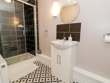 A bathroom with a shower enclosure a sink with cabinet a round mirror and a patterned floor at Ty Coch in Llanberis