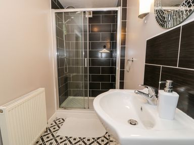 A bathroom with a sink countertop soap dispenser shower with glass doors and black tiled walls at Ty Coch in Llanberis