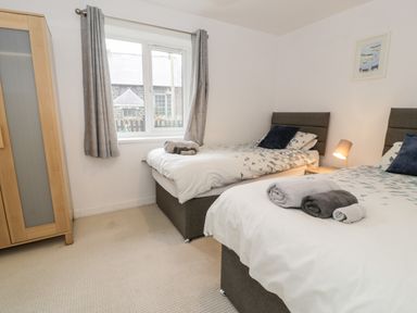 A bedroom with two single beds a wooden wardrobe and a window with grey curtains at Ty Coch in Llanberis
