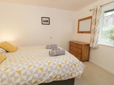 A bedroom with a patterned bedspread a wooden dresser a mirror and a window at Ty Coch in Llanberis