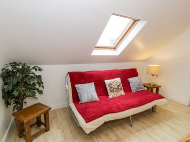 A room with a sofa covered by a red blanket and three cushions under a skylight window at Ty Coch in Llanberis