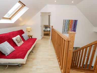 A hallway with a red couch and pillows next to a wooden railing and stairs at Ty Coch in Llanberis