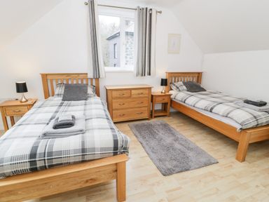 A bedroom with two single beds wooden furniture and a window with striped curtains at Ty Coch in Llanberis