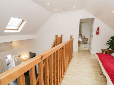 Upstairs hallway with wooden railing overlooking downstairs and a skylight at Ty Coch in Llanberis